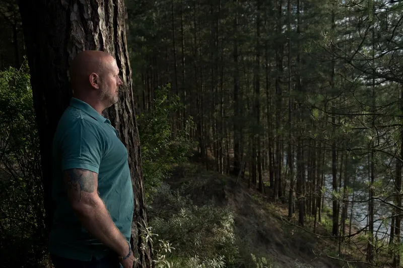 Patrick leunt tegen een boom in het bos en kijkt uit over het water