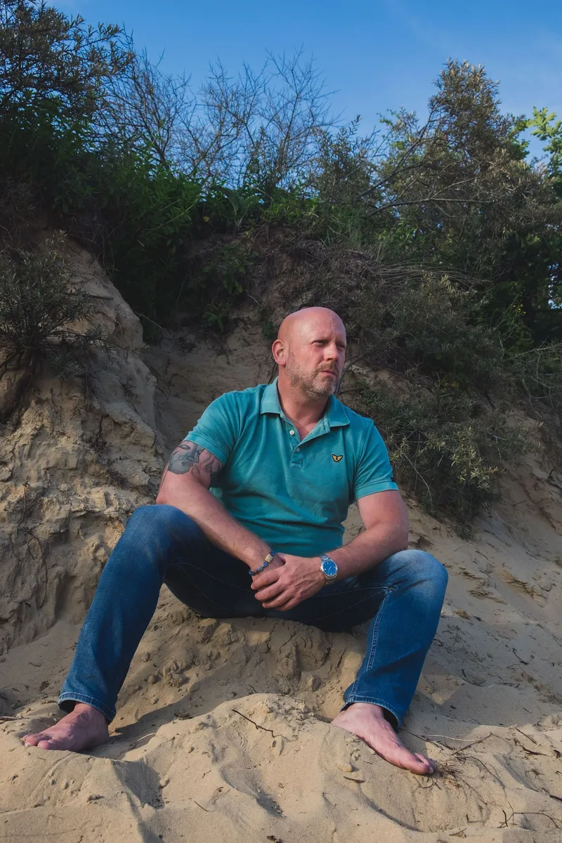 Patrick zit ontspannen in het zand van een duin en kijkt opzij