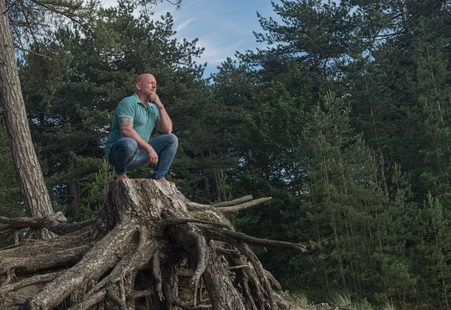 Patrick zit gehurkt op een boomstronk in het bos en kijkt peinzend in de verte