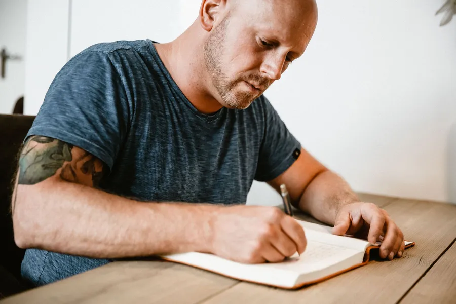 Patrick schrijft geconcentreerd in een notitieboek aan tafel