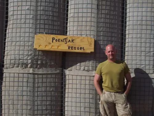Patrick in uitzendtenue bij het houten bord "Poentjak Resort" op het kamp