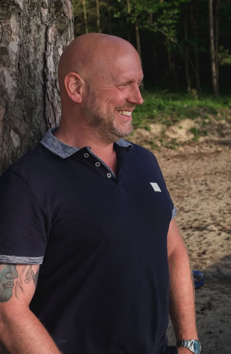 Patrick Scholten lacht, leunend tegen een boom