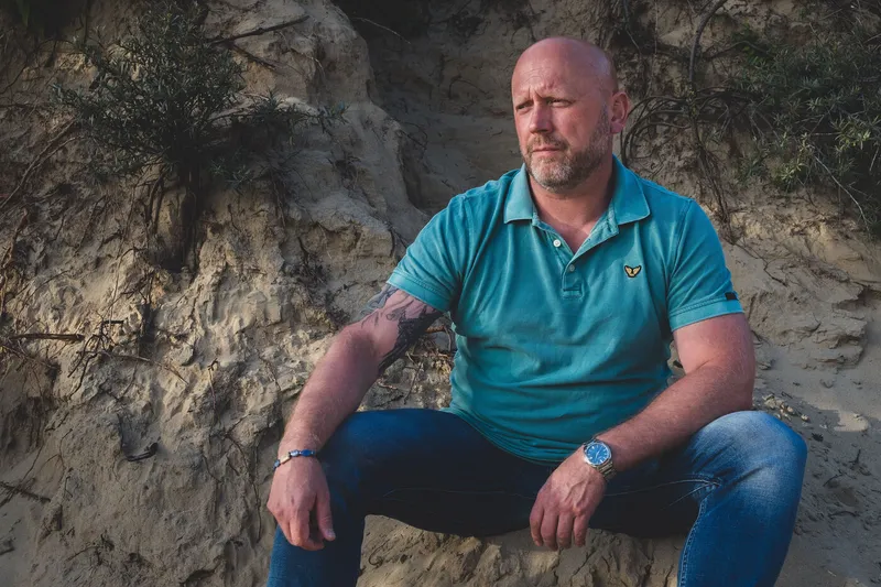 Patrick zit ontspannen op een zandheuvel in de natuur