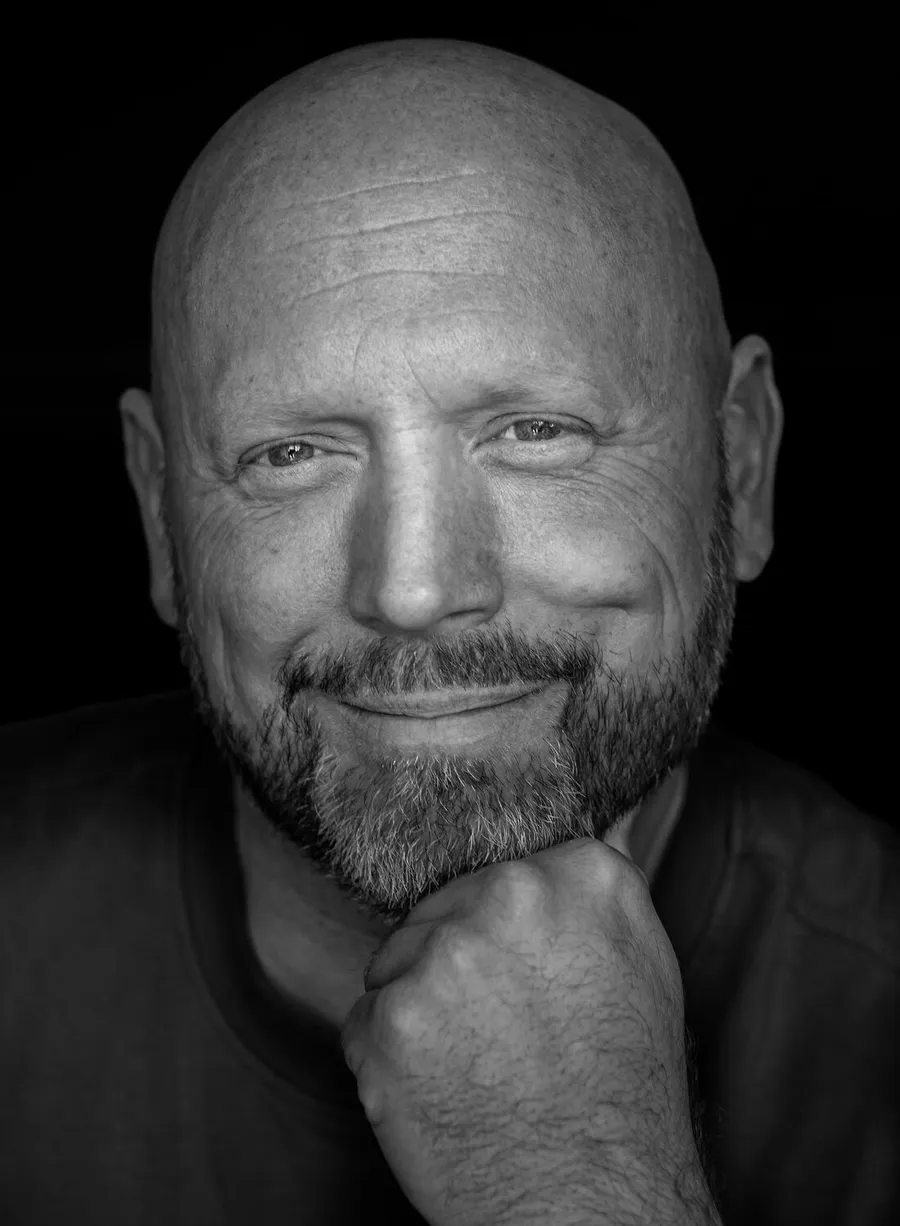Patrick Scholten, lachend portret in zwart-wit, kin op zijn hand