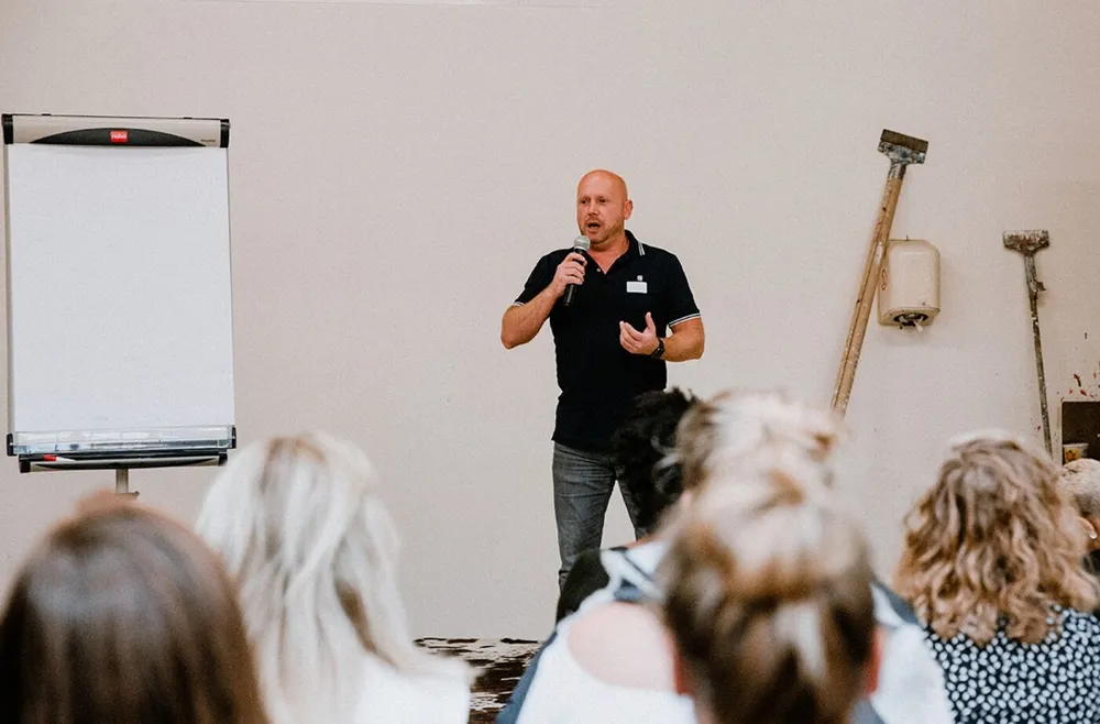 Patrick staat met microfoon voor een zaal tijdens een zaalsessie